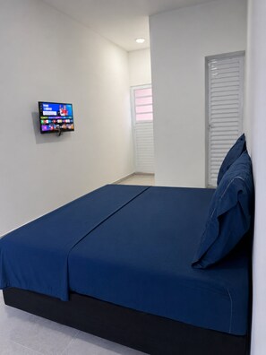 A bedroom with a bed, a television mounted on the wall, and a window with blinds.