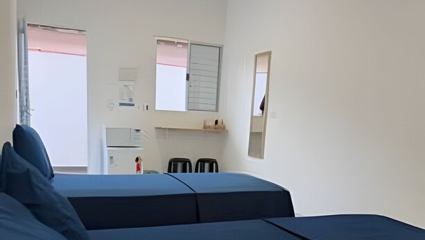 Quarto com cama, escrivaninha e cadeira. Há uma janela e um espelho na parede.