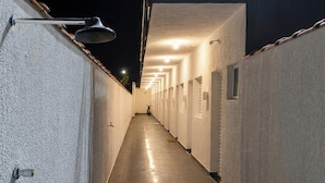 Um corredor com várias portas de um lado e um luminário fixado na parede do outro.