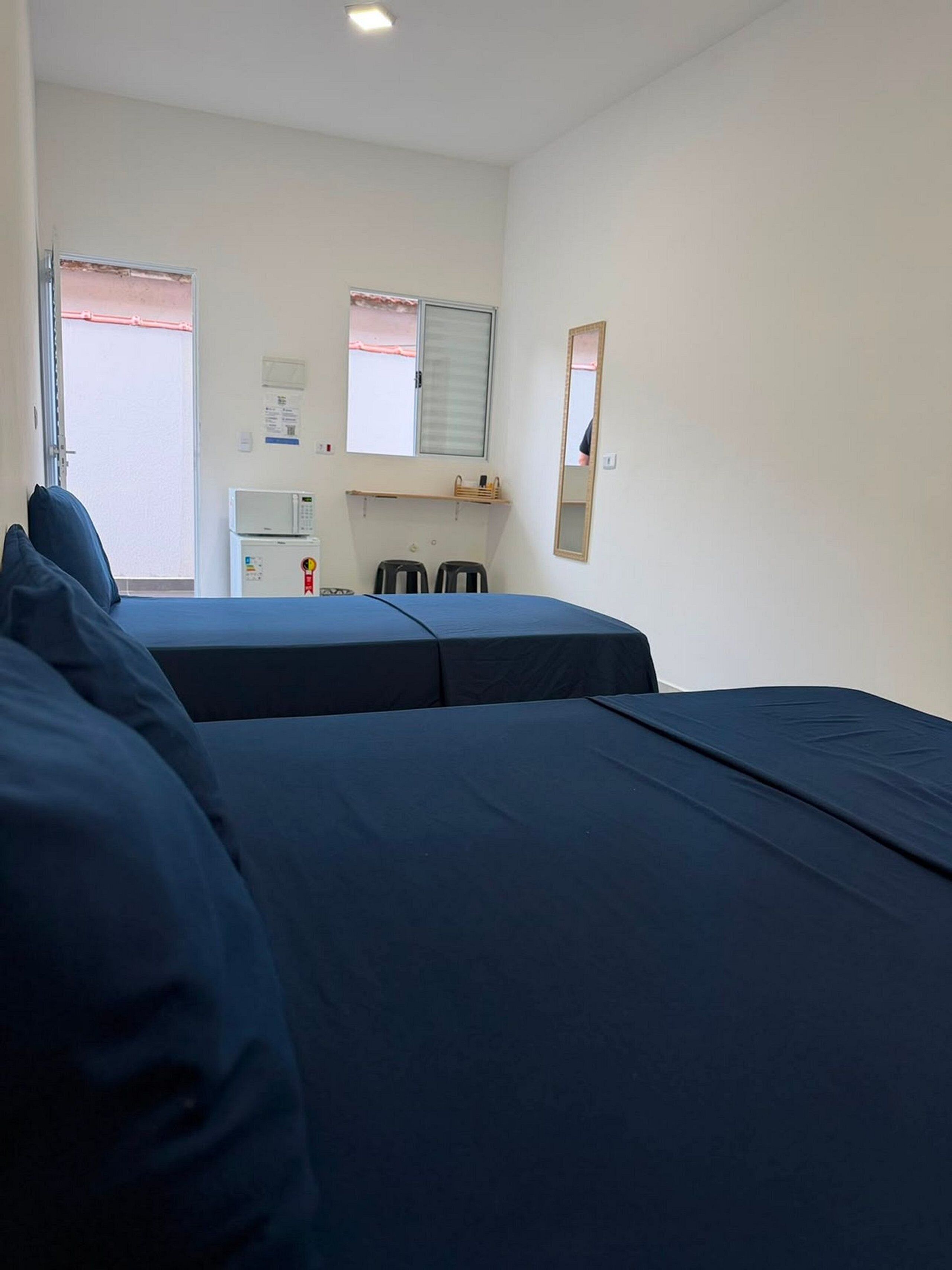 A room with two beds, a microwave, a small table, and a window with blinds.