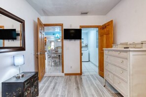 A hallway with a wooden dresser, a TV, and a door leading to a kitchen. - Pet-Friendly Daytona Beach Home Near the Beach (Daytona Beach)