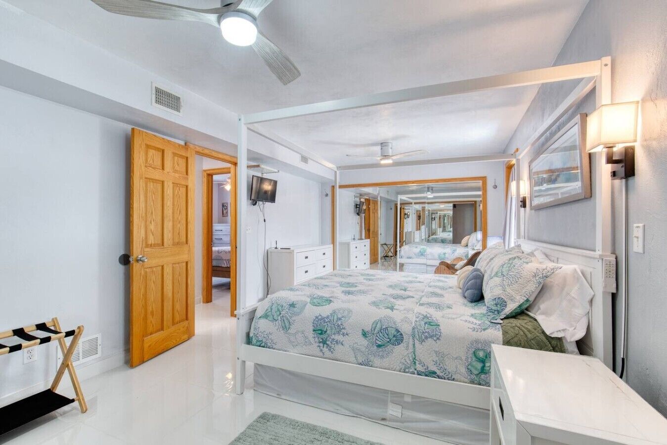 A bedroom with a bed, a TV, a ceiling fan, and a door leading to another room.