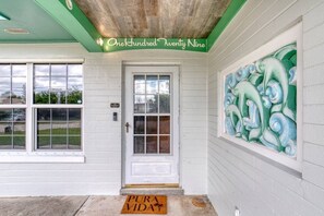 A building entrance with a white door, a green awning, and a decorative wall mural. - Pet-Friendly Daytona Beach Home Near the Beach (Daytona Beach)