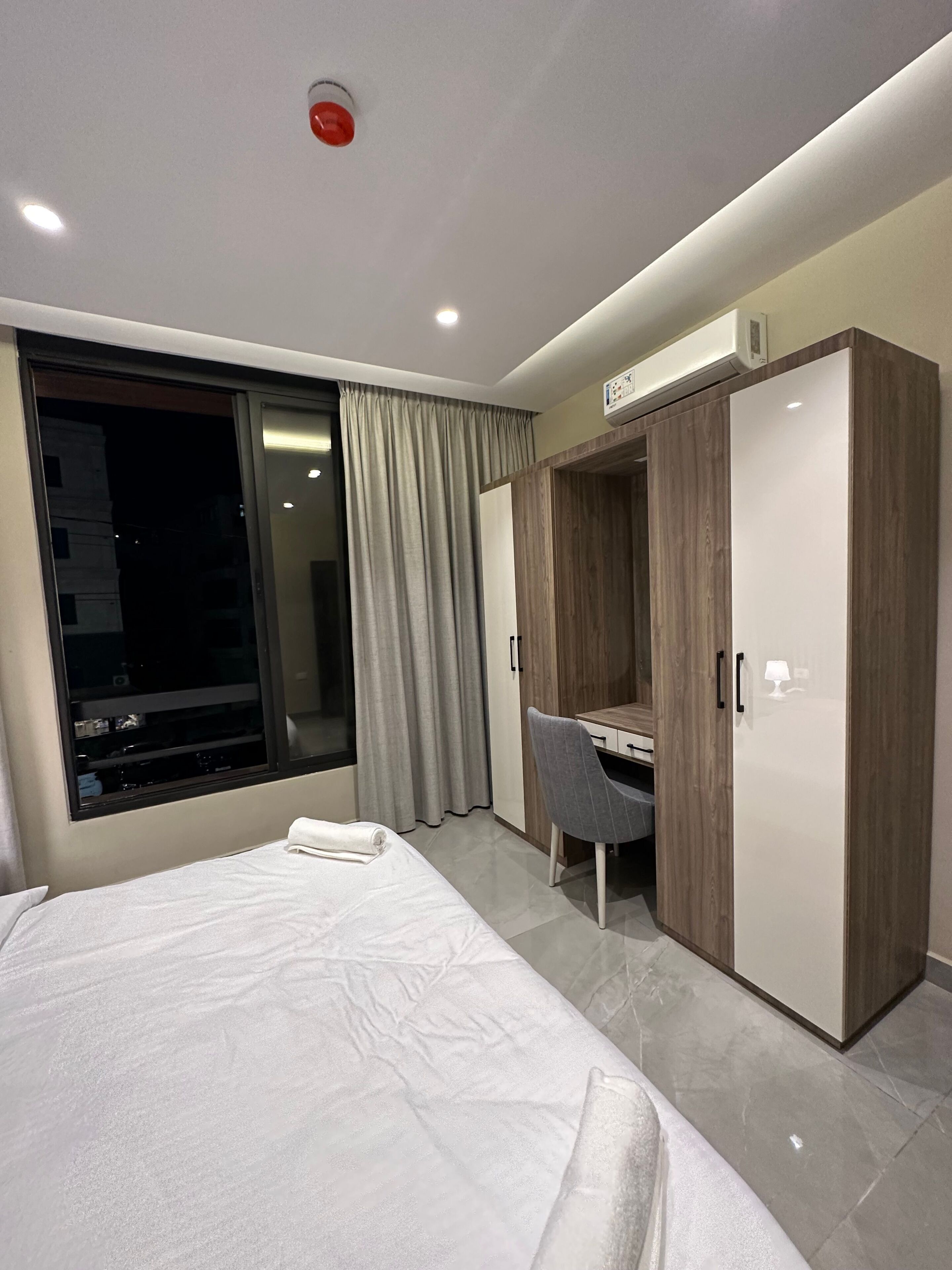 A hotel room with a bed, a desk, a wardrobe, and a window with curtains.
