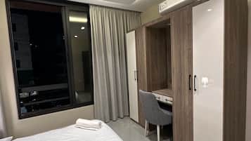 A hotel room with a bed, a desk, a wardrobe, and a window with curtains.