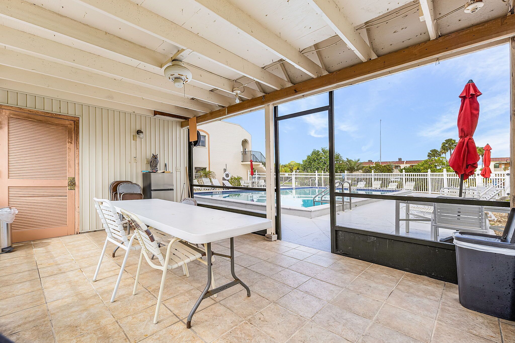 Un patio abrité avec une piscine, une table et des chaises, ainsi qu’une poubelle.