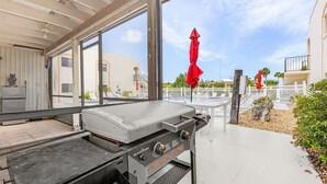 An outdoor grill area with a view of a pool and a white fence. - Adorable 2 Bedroom Condo - Pool & Prime Location (Fort Myers)
