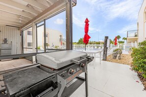 An outdoor grill area with a view of a pool and a white fence. - Adorable 2 Bedroom Condo - Pool & Prime Location (Fort Myers)