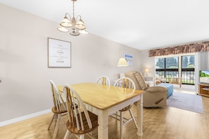 A dining area with a wooden table and chairs, a sofa, and a view of the outdoors through large windows. - Adorable 2 Bedroom Condo - Pool & Prime Location (Fort Myers)