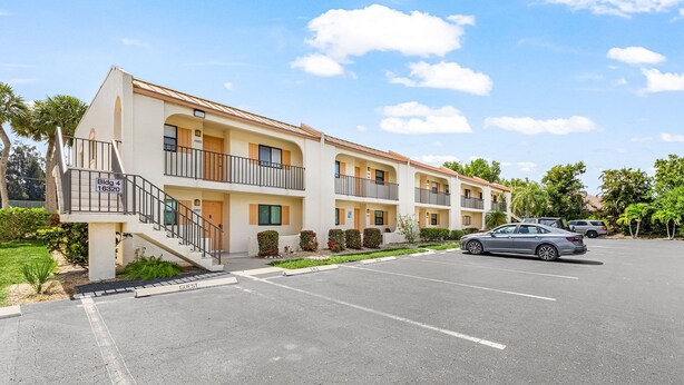 A multi-story hotel with a parking lot, a guest entrance, and a clear sky. - Adorable 2 Bedroom Condo - Pool & Prime Location (Fort Myers)