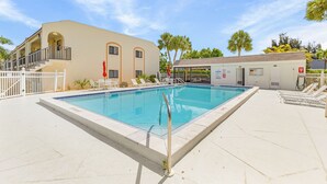 A swimming pool with a metal handrail, a covered area with a door, and a building with a beige facade and arched windows. - Adorable 2 Bedroom Condo - Pool & Prime Location (Fort Myers)