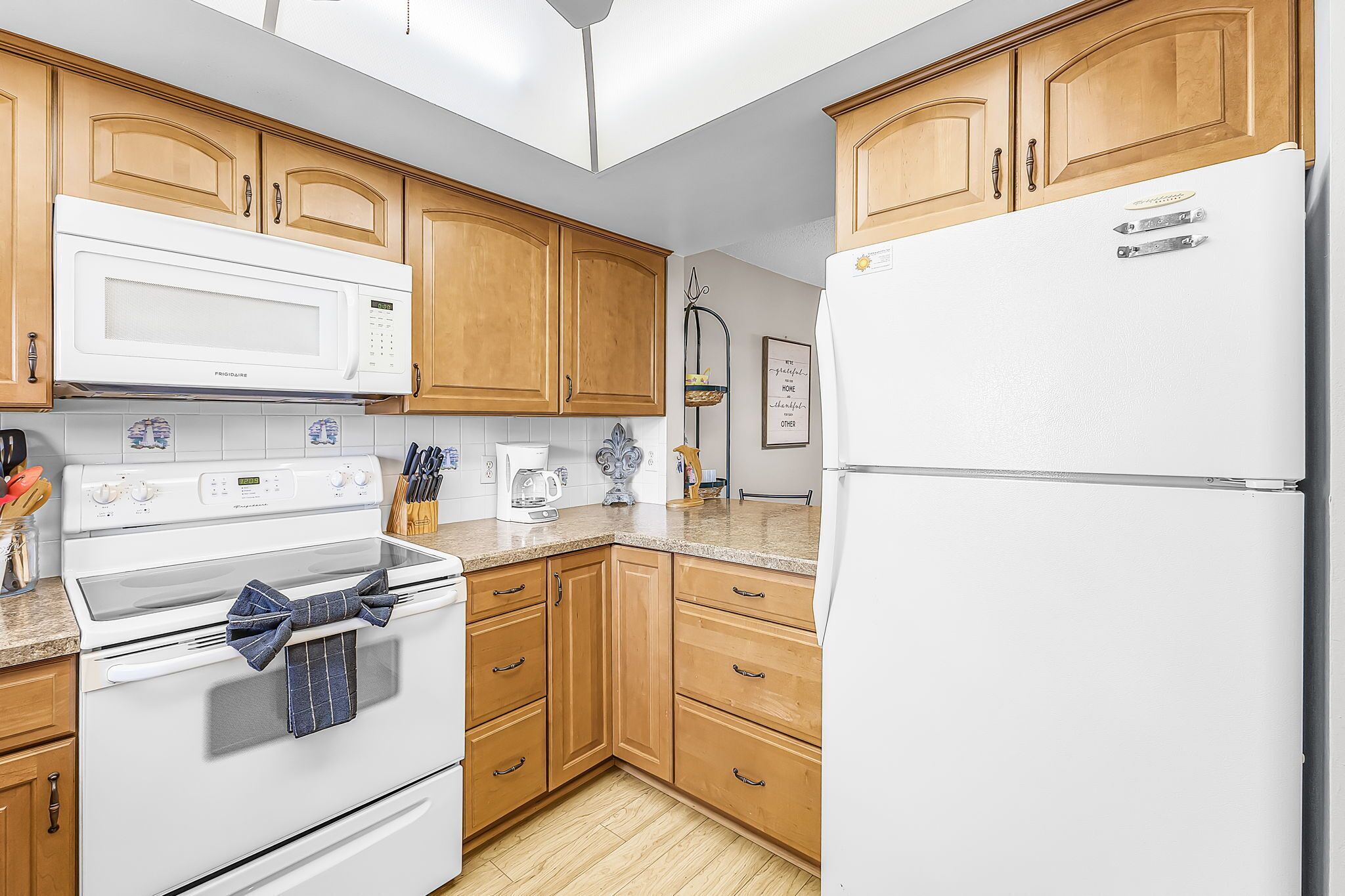 Una cocina con armarios de madera, un refrigerador blanco, un microondas, una estufa y una cafetera.