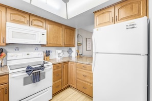 A kitchen with wooden cabinets, a white refrigerator, a microwave, a stove, and a coffee maker. - Adorable 2 Bedroom Condo - Pool & Prime Location (Fort Myers)