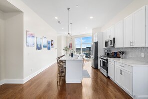 A modern kitchen with white cabinetry, a central island, and a dining area with chairs. - Warm & Modern 3Bdrm NoLibs Condo - Sleeps 7! (Philadelphia)