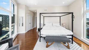 A modern bedroom with a four-poster bed, a bench, and a view of the city through large windows. - Warm & Modern 3Bdrm NoLibs Condo - Sleeps 7! (Philadelphia)