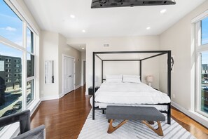 A modern bedroom with a four-poster bed, a bench, and a view of the city through large windows. - Warm & Modern 3Bdrm NoLibs Condo - Sleeps 7! (Philadelphia)