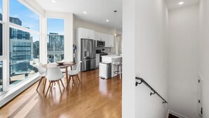 A modern kitchen with white cabinets, stainless steel appliances, and a dining area with a wooden table and white chairs. - Warm & Modern 3Bdrm NoLibs Condo - Sleeps 7! (Philadelphia)