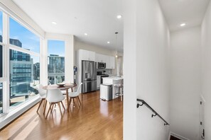 A modern kitchen with white cabinets, stainless steel appliances, and a dining area with a wooden table and white chairs. - Warm & Modern 3Bdrm NoLibs Condo - Sleeps 7! (Philadelphia)