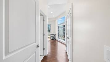 A hallway with white doors, a wooden floor, and a view of a building through a window.