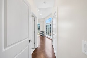 Un pasillo con puertas blancas, suelo de madera y vista a un edificio a través de una ventana.