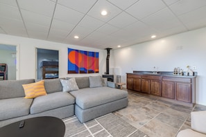 A modern living room with a sectional sofa, a small coffee table, and a kitchen area with wooden cabinets and a countertop. - Lake Michigan Retreat! Beautiful Views & Amazing Amenities (Ludington)