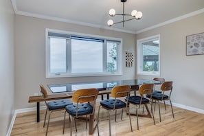 A dining area with a glass-top table, six chairs, and a modern chandelier. - Lake Michigan Retreat! Beautiful Views & Amazing Amenities (Ludington)