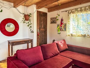 A red sofa, a wooden table, a mirror, and a window with a curtain. - Casa Serena by Interhome (Mergoscia)