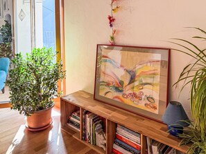 A room with a wooden bookshelf, a potted plant, and a framed abstract painting on the wall. - Casa Serena by Interhome (Mergoscia)