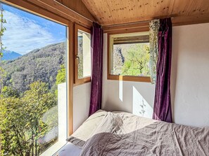 A bedroom with a large window, a bed, and a view of a forested area. - Casa Serena by Interhome (Mergoscia)