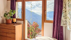 Ein Schlafzimmer mit einem hölzernen Schminktisch, einer Nachttischlampe, einem Bett und Bergblick durch eine Schiebetür.