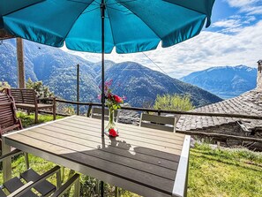 A wooden table with a vase of flowers, a blue umbrella, and a view of snow-capped mountains. - Casa Serena by Interhome (Mergoscia)