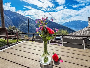 A wooden table with a glass vase containing flowers and a red rose, set against a mountainous backdrop. - Casa Serena by Interhome (Mergoscia)