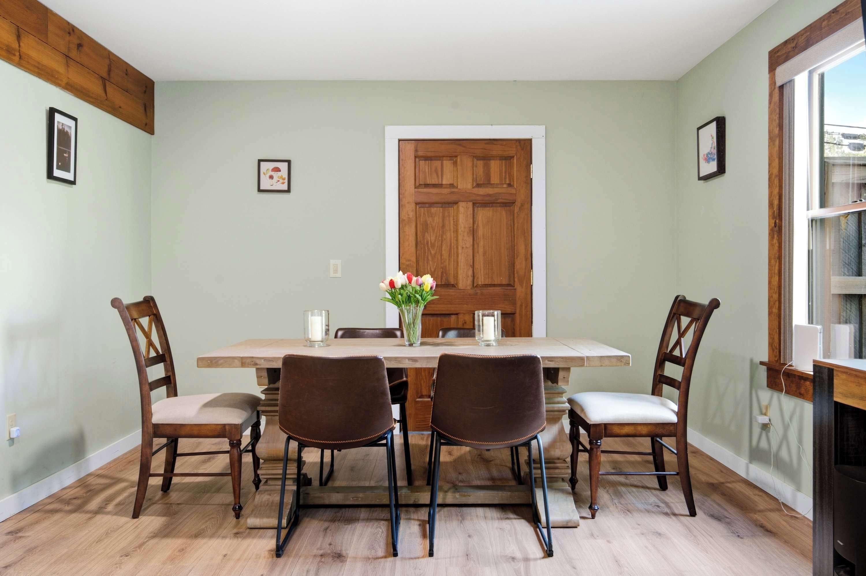 Comedor con una mesa de madera, cuatro sillas, un florero con flores y una puerta de madera.