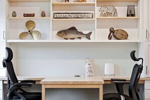 A desk with two chairs, a wooden table, and shelves with decorative items including a fish, shells, and a sign that reads 'SALMON CROSSING'. - Rangeley Lakefront 3BR | Private Dock, Dogs OK (Rangeley)