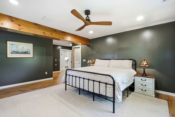 A bedroom with a bed, bedside tables, a ceiling fan, and a door leading to another room.