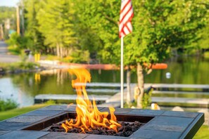 A fire pit with flames, surrounded by a body of water and greenery.