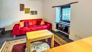 Ett vardagsrum med en röd soffa, ett soffbord i trä, en tv och konstverk på väggen.