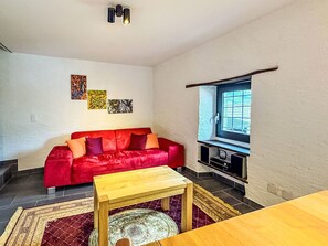 Ein Wohnzimmer mit einem roten Sofa, einem Holztisch, einem Fernseher und Kunstwerken an der Wand.