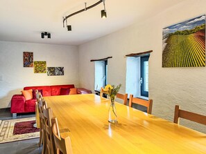 Een eetgedeelte met een houten tafel, stoelen, een rode bank en kunstwerken aan de muur.