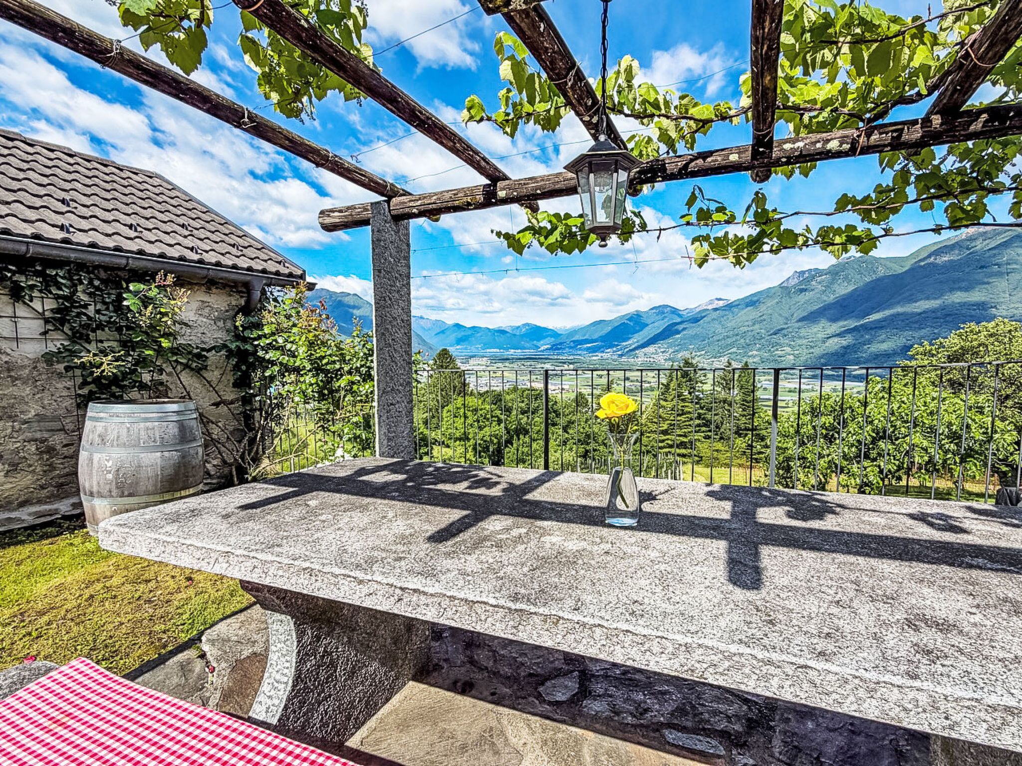 A stone bench with a metal railing, a potted plant, and a table with a checkered tablecloth.