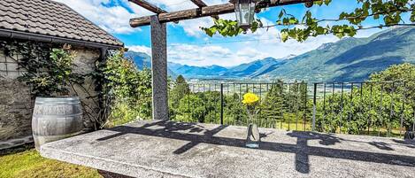 A stone bench with a metal railing, a potted plant, and a table with a checkered tablecloth.