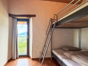 A bunk bed room with a wooden ladder, a window with curtains, and a view of greenery and mountains. - Rustico Martina by Interhome (Bellinzona)
