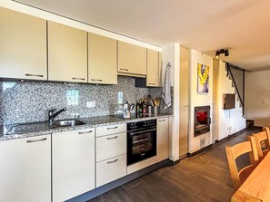 A modern kitchen with granite countertops, stainless steel appliances, and a dining area with wooden chairs. - Rustico Martina by Interhome (Bellinzona)