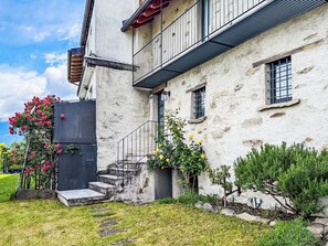 A two-story building with a stone facade, a balcony, and a small garden area with flowers and shrubs. - Rustico Martina by Interhome (Bellinzona)