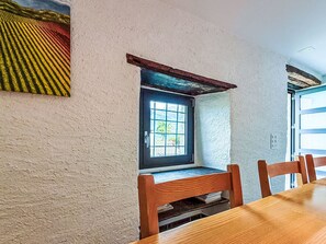 Ein Zimmer mit Holztisch, Stühlen, einem Fenster mit Aussicht und einer strukturierten Wand.