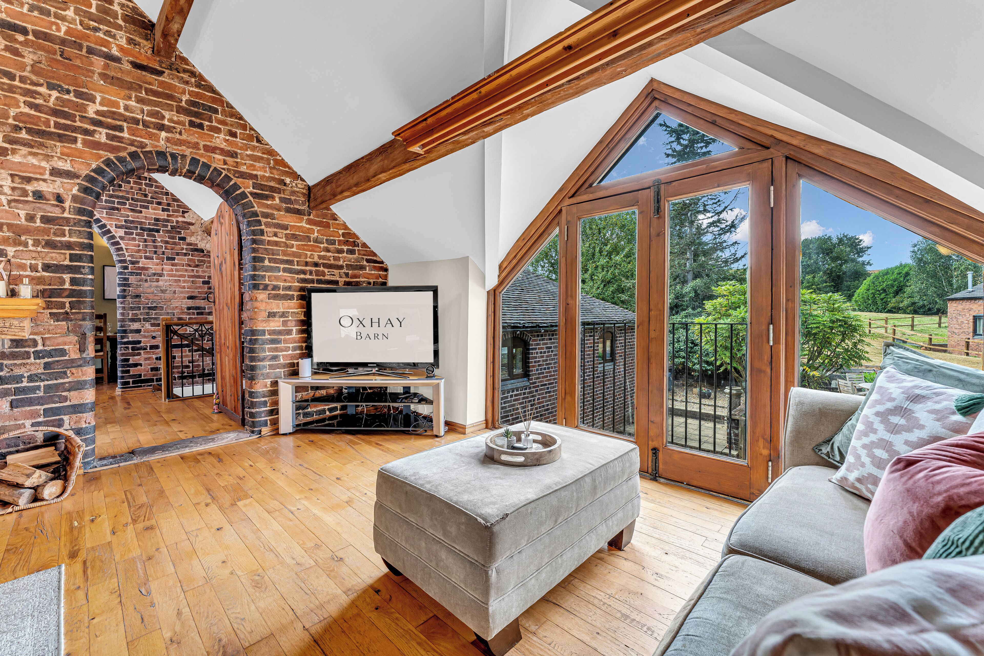 A spacious living room with a brick fireplace, a television, and a large window offering a view of the outdoors.