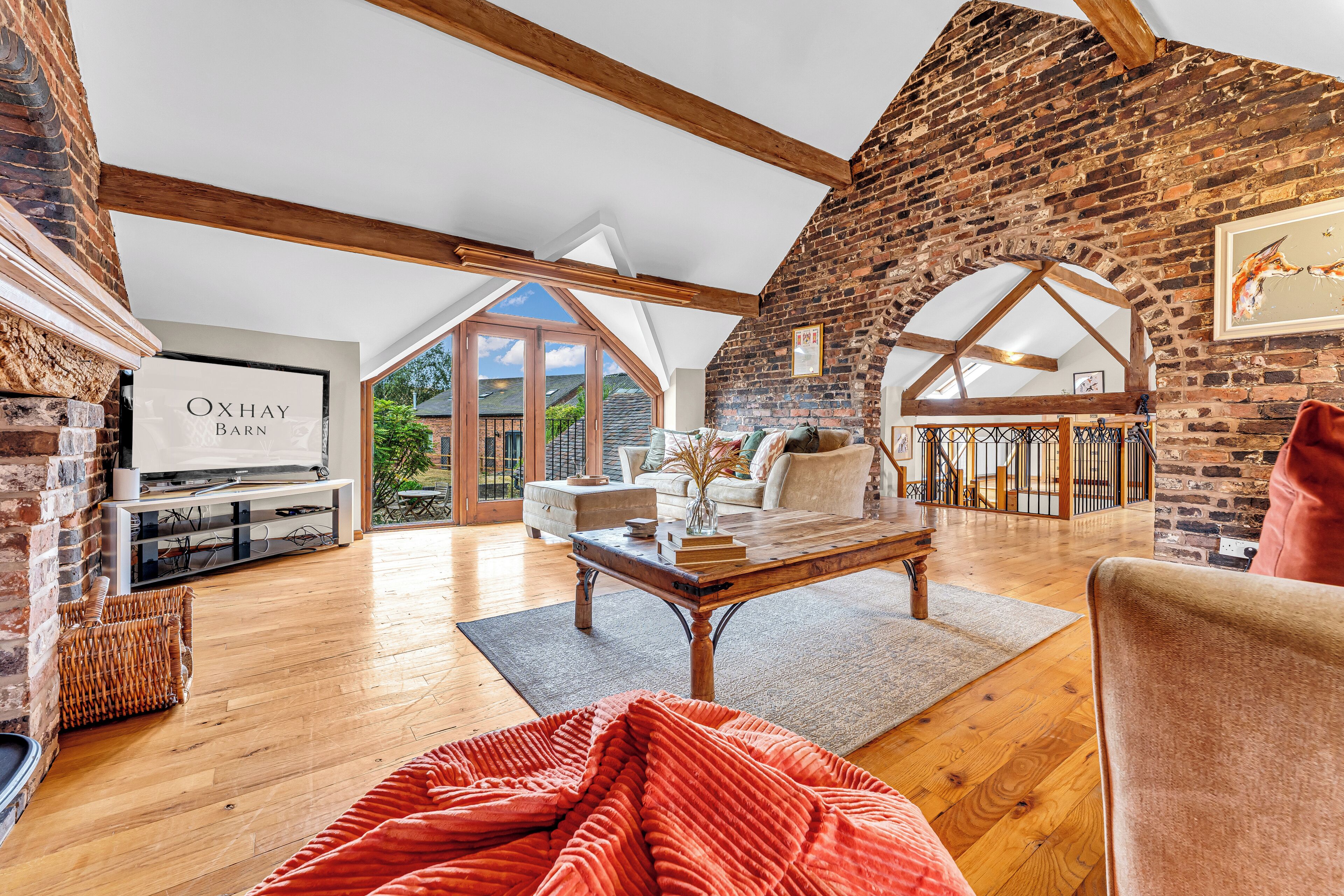 A spacious loft with exposed wooden beams, a brick wall, and a large window offering a view of the outdoors.