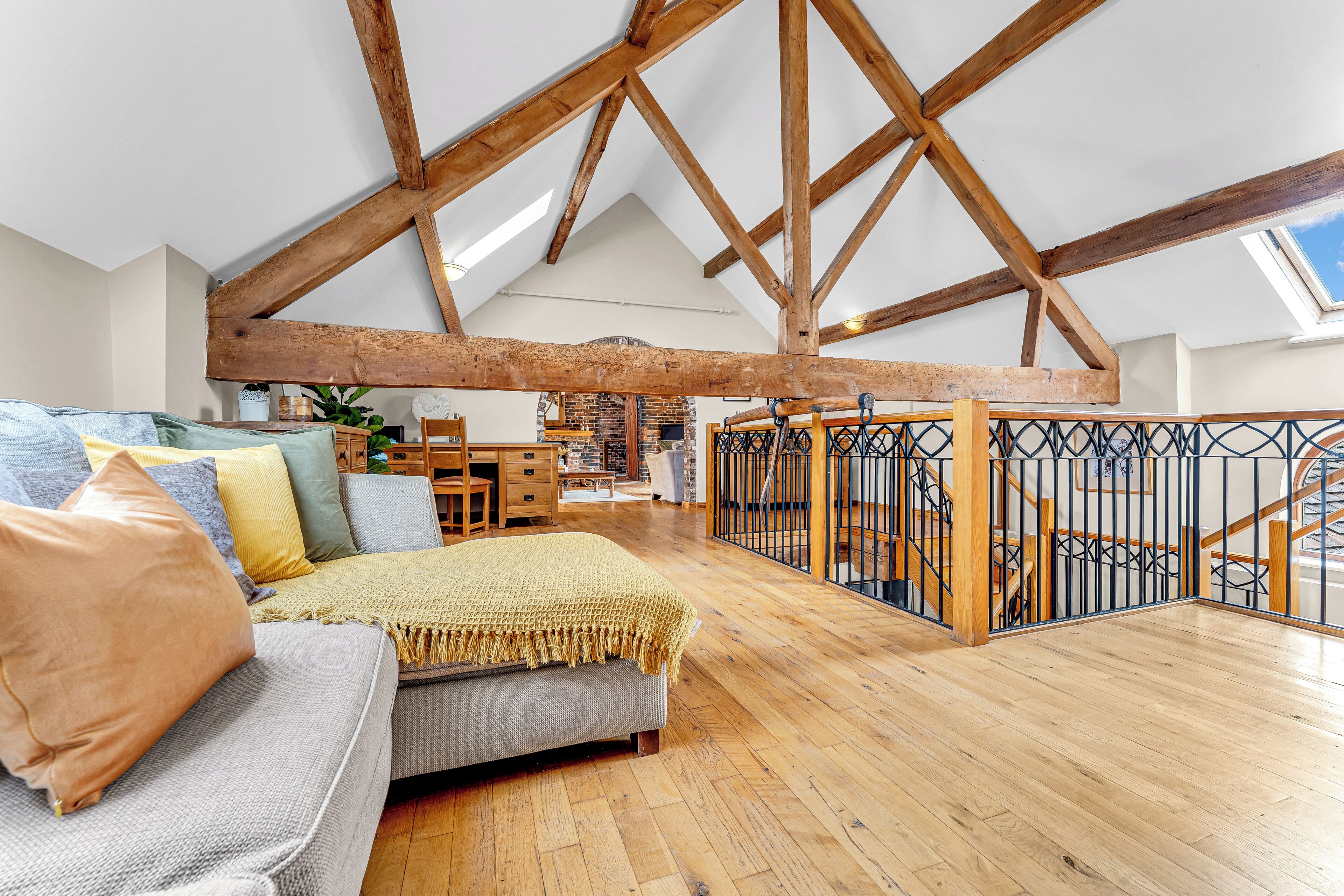 A spacious loft with exposed wooden beams, a cozy seating area with a sofa and cushions, and a view of the sky through a skylight.