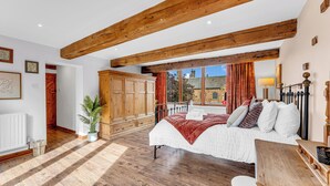 A bedroom with a large bed, wooden beams, a view to the outside, and a wardrobe.