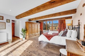 A bedroom with a large bed, wooden beams, a view to the outside, and a wardrobe. - Oxhay Barn Luxury Stay, Sleeps 14 • Hot Tub • Gym (Newcastle Under Lyme)